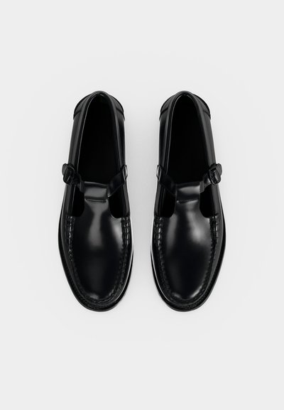 Paire de mocassins noirs en cuir avec brides à boucle et détails cousus, vus de dessus sur fond blanc uni.