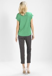 Top verde de manga corta combinado con pantalones negros estampados. El top es suave y holgado; los pantalones tienen un corte ajustado con un patrón de diamantes.