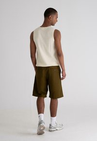Light beige ribbed tank top and olive green shorts, viewed from the back. The tank has a crew neck; shorts feature two back pockets.
