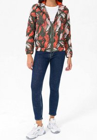 Vuoritettu vihreä takki, jossa on punavalkoinen trooppinen kukkakuosi, vetoketju edessä ja kiinnitetty huppu. Yhdistetty tummiin kapeisiin farkkuihin ja valkoisiin tennareihin.