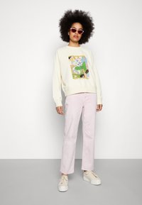 Sweatshirt creme com um gráfico floral colorido, combinado com jeans retos cor-de-rosa claros e ténis brancos de plataforma. Óculos de sol redondos cor-de-rosa.