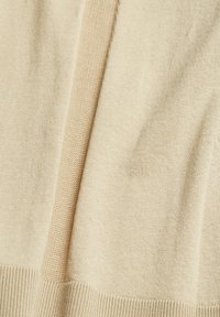 Tissu tricoté beige avec ourlet en côtes et un détail de couture texturée verticale au centre.