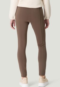 Leggings moulants marron en matière extensible, présentant une texture lisse, avec une taille haute et un design sans coutures.