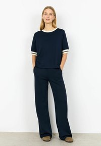 Mornarsko modra zgornja majica z sproščenim krojem in manšetami z belimi črtami, združena z ujemajočimi širokimi hlačami. Mehki material z gladko teksturo.