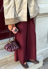 Bordo široke hlače s prugicami, bež jakna s kordurojskimi manšetami, temno rjava torba in cvetlična etui za telefon.