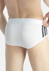 Bóxers blancos hechos de una tela suave, con un ajuste ceñido, una cinturilla blanca y tres rayas verticales negras a los lados.