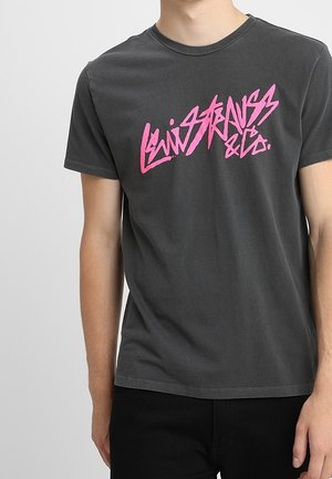 Szara bawełniana koszulka z krótkim rękawem, na której przodzie znajduje się duży różowy napis "Levi Strauss & Co.". Gładki tył, standardowy okrągły dekolt.