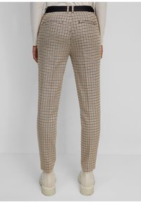 Pantalon à carreaux beige, marron et noir ; coupe slim avec une texture lisse, doté de deux poches arrière et d'une ceinture noire en accent.