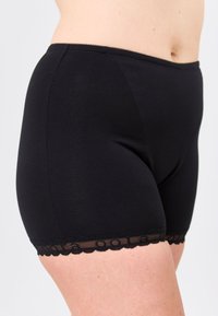 Mustat venyvät puuvillahousut, joissa on sileä pinta ja koristeellinen pitsireuna helmassa. Ihonmyötäinen malli, joka tarjoaa keskikorkeaa peittävyyttä.