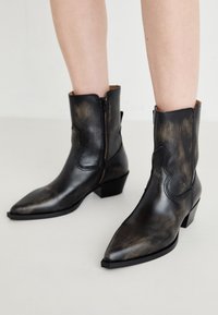 Bottes noires en cuir à lacets avec des bouts pointus, une fermeture éclair latérale et un petit talon empilé. Elles présentent une finition vieilli et une couture western délicate.