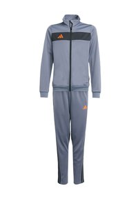 Traje deportivo gris hecho de material ligero, con un panel en el pecho negro, chaqueta con cremallera, pantalones a juego y acentos en logo naranja.