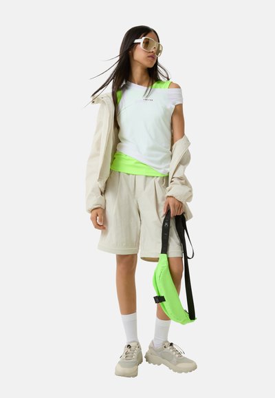 Sporty outfit featuring a white tank, neon green accents, beige shorts, and a light jacket. Accessories include oversized sunglasses and a green bag.