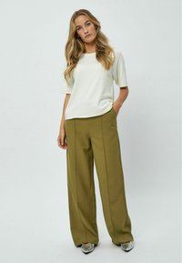 Haut blanc à manches courtes avec un col arrondi, associé à un pantalon large vert olive avec des détails de couture centrale et des accents métalliques sur les chaussures.