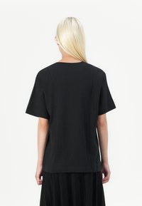 T-shirt nera a maniche corte con vestibilità rilassata e scollo tondo, realizzata in tessuto morbido, vista da dietro. Design semplice, senza loghi visibili.