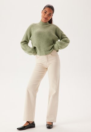 Maglione a coste verde chiaro con collo alto, abbinato a pantaloni beige a gamba larga e ballerine nere. Design semplice, texture morbida.