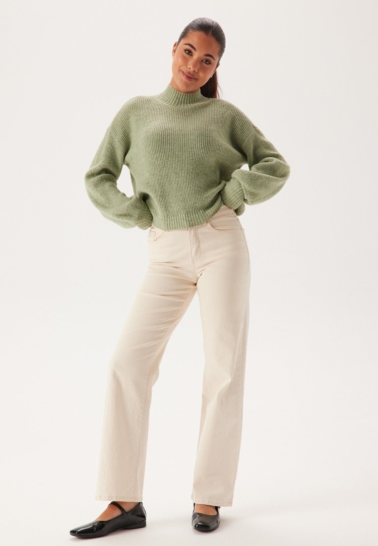 Lichtgroene geribbelde trui met hoge hals, gecombineerd met beige wijde broek en zwarte flats. Eenvoudig ontwerp, zachte textuur.