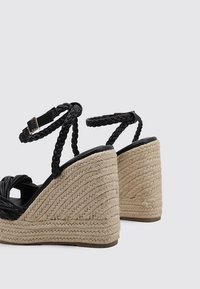 Schwarze geflochtene Keilsandalen mit einem strukturierten, braunen geflochtenen Absatz. Verfügt über einen Knöchelriemen mit einer Schnallenverschluss. Offene Zehen-Design.