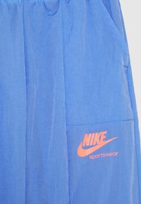 Modré lehké šortky vyrobené z hladké tkaniny, s oranžovým logem Nike na boční kapse a elastickým pasem.