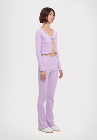 Lilac ribbed two-piece set featuring a cropped top with a front tie and flared pants with scalloped hems. Material has a soft texture.