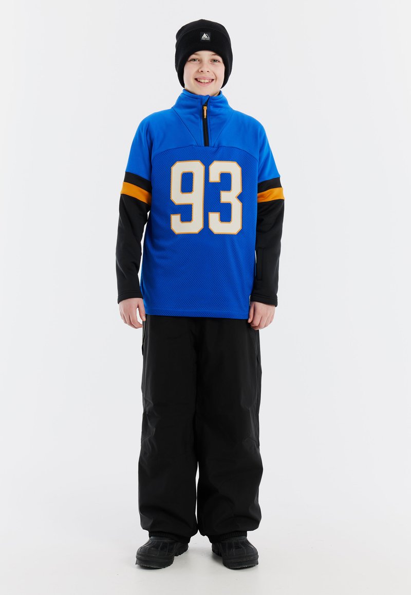Niebieski sweter z półzamkiem, z dużym numerem 93 w białym kolorze, czarnymi rękawami z pomarańczowymi paskami, w zestawie z czarnymi spodniami narciarskimi i butami.
