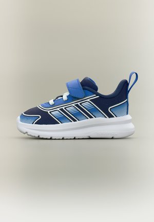 Baskets de sport bleu marine et bleu clair avec semelle blanche, fermeture Velcro, languette au talon et accents rayés blancs, présentées en vue latérale.