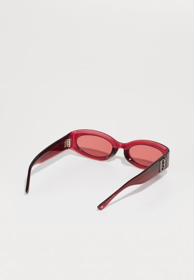 Red sunglasses with oval lenses. Transparent red frames with a darker gradient at the temples. Metallic accents on the side.