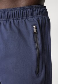 Navy blue athletic shorts with an elastic waistband and a zippered side pocket, featuring a smooth fabric texture and minimalistic design.