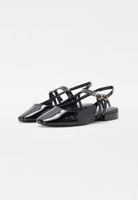 Ballerine in vernice nera con punta a punta, tacco basso e cinturini incrociati. Presentano piccoli dettagli in tono oro sui cinturini.