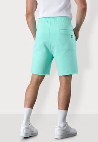 Shorts en sweat vert menthe avec un waistband élastique, une poche arrière et des détails effilochés au niveau de l'ourlet. Associés à des sneakers blanches et des chaussettes.