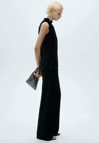 Un top fără mâneci din cotele negre și pantaloni evazați, asortați cu o geantă mică speckled alb-negru și cercei mari.