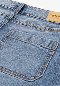 Jeans de mezclilla azul claro con costuras naranjas en contraste. Presenta un bolsillo trasero con una textura sutil y una etiqueta de cuero con la marca en la cintura.