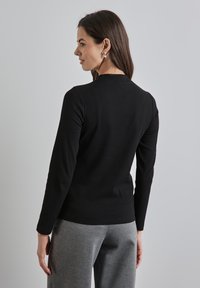 Schwarzes, geripptes Langarmoberteil mit Rundhalsausschnitt, enganliegender Passform und strukturiertem Stoff; kombiniert mit grauen Sweatpants für einen lässigen Look.