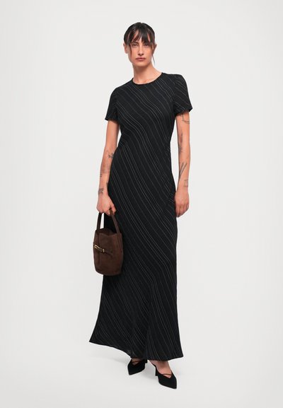 Black, short-sleeve dress with a long, flowing design, featuring white diagonal stripes. Paired with a brown suede handbag and black pointed shoes.