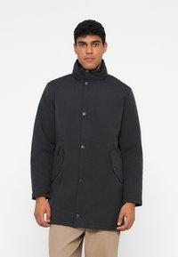 Μαύρο, μονωμένο μπουφάν παρκά με ψηλό γιακά, κλείσιμο με κουμπιά και πλαϊνές τσέπες με φερμουάρ. Υφή υφάσματος, μήκους μέχρι το γόνατο.