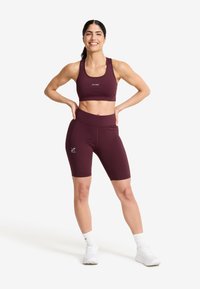 Burgundy träningstopp med kort längd och högmidjade cykelshorts gjorda av elastisk tyg. Har logotypdetaljer och en figurnära design.