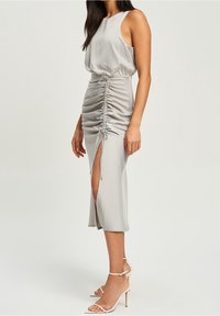 Silkig grå midiklänning med sidofåll, justerbar knytning och slits till låret; ärmlös med rund halsringning.