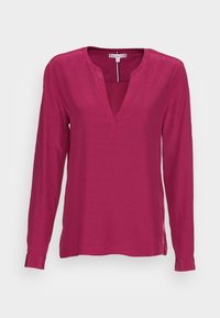 Haut à manches longues en magenta vif avec un décolleté en V, fabriqué dans un tissu lisse. Dispose d'une fente latérale discrète à l'ourlet et de manches à poignets.