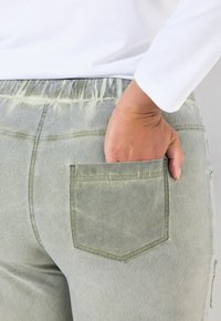 Pantalons vert clair à taille élastique avec une poche arrière au design carré. Le matériau a une apparence légèrement texturée.