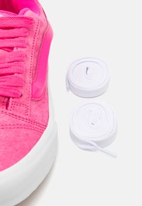 Zapatilla rosa con parte superior texturizada, suela de goma blanca y cordones planos blancos a los lados. Destaca por su color vibrante y el contraste de materiales.