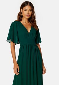 Robe longue verte avec un décolleté en V profond et des manches évasées. Fabriquée en tissu lisse, elle présente une taille cintrée et une jupe fluide.