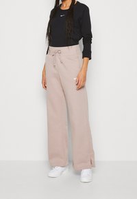 Svart långärmad tröja med en vit Nike-logga, ihopparad med ljusrosa vida mjukisbyxor med dragsko och sidoklipp. Vita sneakers.