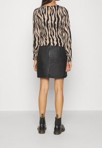 Haut à manches longues avec un imprimé zèbre beige et noir, associé à une mini-jupe en cuir noire et des bottines noires avec des accents jaunes.