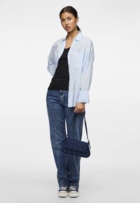 Lys blå skjorte med knapper, svart linne, blå jeans og mørkeblå skulderveske med nagler. Avslappet fottøy fullfører antrekket.