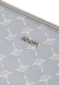 Portafoglio in pelle testurizzata azzurro chiaro con un motivo floreale ripetuto e un logo "JOOP!" in argento sulla parte anteriore. Chiusura a zip lungo la parte superiore.