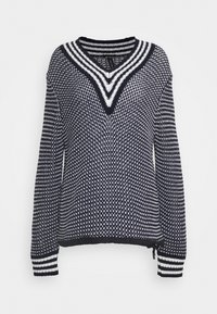 Pull en tricot bleu marine et blanc avec un col en V, des manches longues et des poignets rayés. Présente un motif texturé sur l'ensemble et des zips sur les côtés.