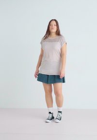 Helles beiges T-Shirt mit kurzen Ärmeln und strukturiertem Spitzen-Detail, kombiniert mit einem Jeans-A-Linien-Rock und weißen Knöchelsocken, die mit schwarzen Sneakers getragen werden.