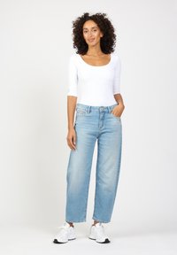 Light blue wide-leg jeans with five pockets, slight fading, and a traditional button and belt loop design. Paired with a white fitted top.