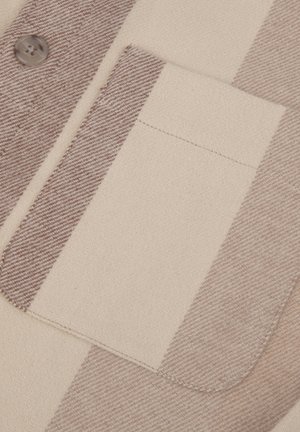 Tessuto a righe beige e marrone con una superficie liscia, dotato di una piccola tasca sul petto e un dettaglio con bottone rotondo.