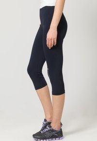 Marina capri leggings i stretchmaterial med en åtsittande design, som har nätpartier och en logotyp på sidan. Paret med svarta sneakers.