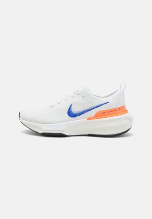 Scarpa sportiva bianca con swoosh blu, accento arancione, parte superiore in mesh leggero, suola ammortizzata e suola in gomma nera.